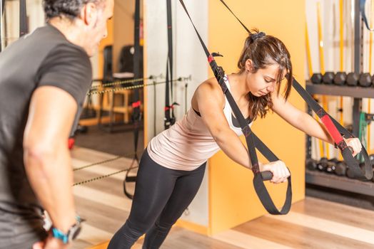 Sportswoman doing exercise with trx fitness straps in gym. Concept of exercises with equipment in gym.