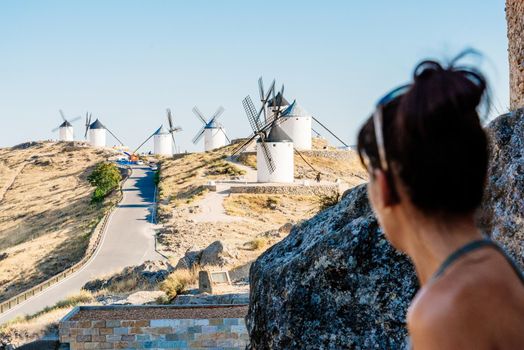 Selective focus on antique windmills with a woman looking at them from the shadow of a Castle in Consuegra, Toledo, spain