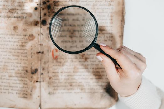 Woman researcher explores antique book with magnifier. Scientific translation of literature. Investigating manuscript with ancient writings. High quality