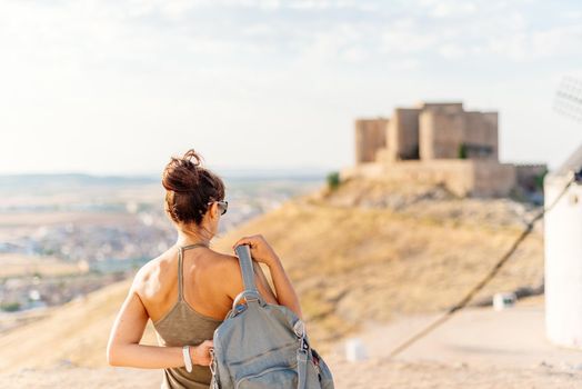 Woman putting a bag while facing the views of a castle on a hill in Toledo, Spain