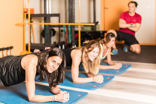 Sportswomen looking at camera doing plank exercise on foam roller with trainer in the gym. Concept of exercises in gym.