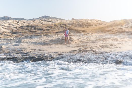 Aerial of female traveler admiring scenic seascape while standing on sand near wavy water and looking for place for putting towel, during vacation in sunny day in Andalusia Spain