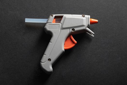 Gray and orange hot glue gun on a dark background