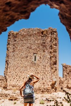 Vertical photo of a young woman wearing a hat looking at the wall of a ruined medieval castle. Almoncid Castle in Spain