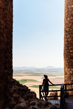 Vertical photo of a woman leaning on a railing between the towers of historic windmills on a hill in Toledo, Spain.