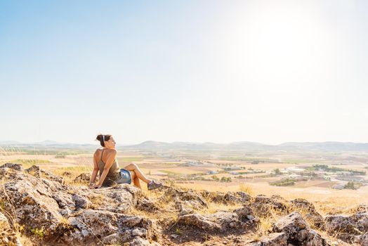 Photo with copy space of a woman sitting on a hill overlooking the fields on the plain on a sunny and windy day in Toledo, Spain