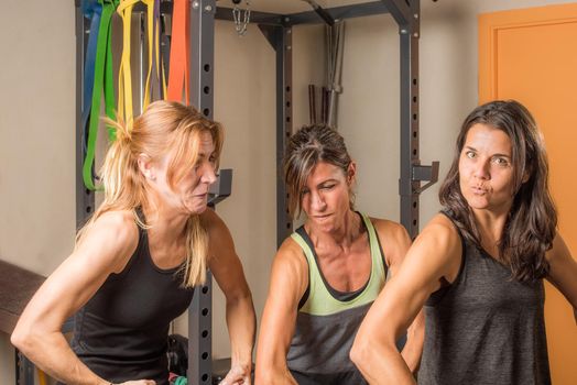 Three sportswoman showing arms muscles in funny way in gym. Concept of people in gym.