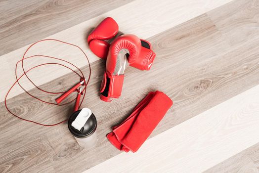 Top view of red boxing gloves, a red rope, a bottle of water and a red towel on a wooden background. Concept of equipment of box.