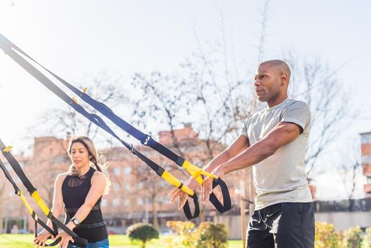 Couple of athletes exercising with trx fitness straps in the park. Adult man and woman exercising outdoors.