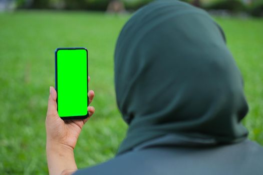 rear view of young women using smart phone with green screen sitting on park ,