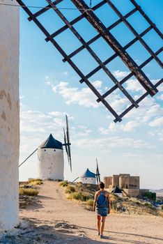 Vertical young woman with a bag walking among old windmills and a castle in Toledo, Spain.