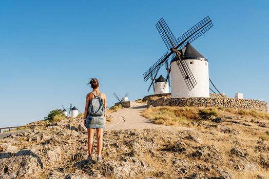 Woman in summer clothes and a bag standing contemplating some ancient windmills in Consuegra, Spain.