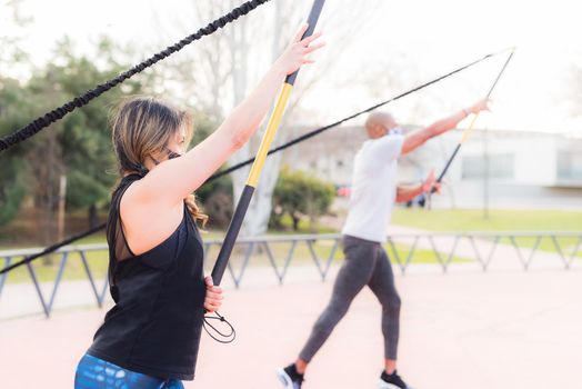 Side view of fitness couple exercising with an elastic gym stick in the park. Multi-ethnic people exercising outside.