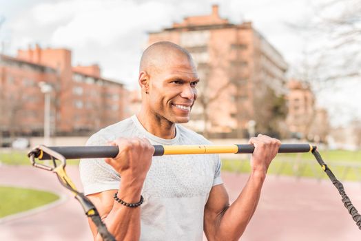 Atlhetic latin sportsman exercising with an elastic gym stick in the park. Hispanic adult man exercising outside.