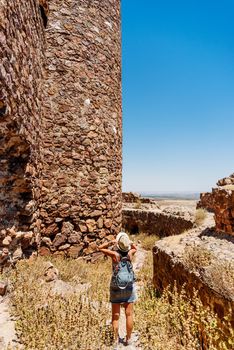 Woman taking his hat and standing in front of the defense stone walls of a medieval castle. Almonacid Castle, Toledo