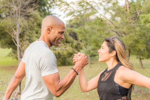 Close up of an ahlete couple exercising by holding with one hand in the park. Multi-ethnic people exercising outside.