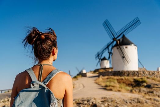 Back of a woman in summer clothes and a bag looking at ancient windmills in Consuegra, Spain.