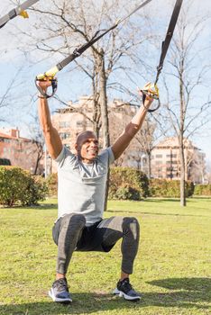 Athlete exercising with trx fitness straps in the park. Adult man exercising outside.