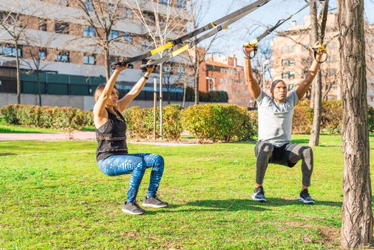 Couple of athletes exercising with trx fitness straps in the park. Adult man and woman exercising outdoors.