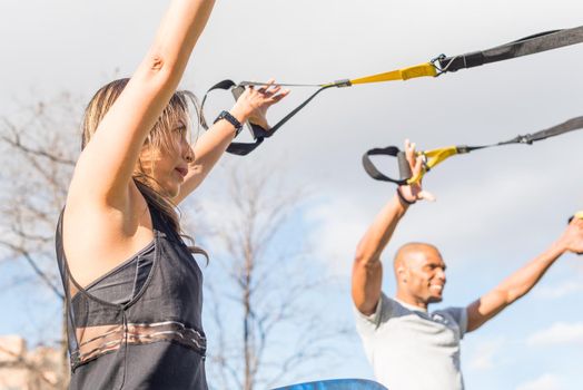 Couple of athletes exercising with trx fitness straps in the park. Adult man and woman exercising outdoors.