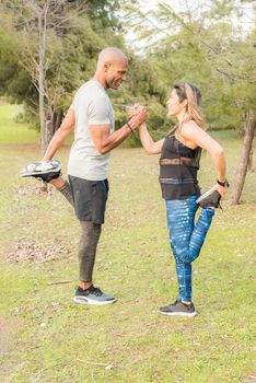 Fitness couple exercising by holding with one hand in the park. Multi-ethnic people exercising outside.