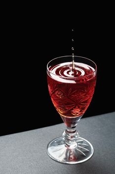 Luxurious cocktail in a crystal goblet with waves of drops on a dark stone background