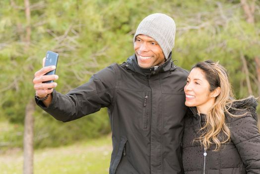 Fitness couple in warm clothes taking a selfie in the park. Multi-ethnic couple outdoors.