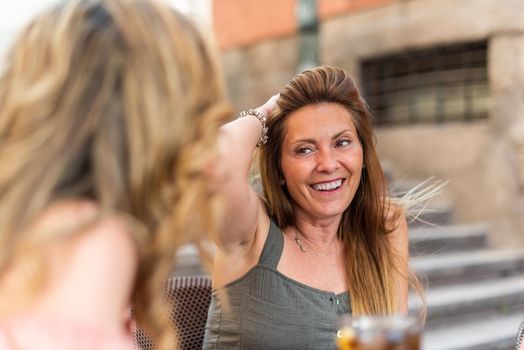 Mature woman in a cafe having drinks with her friends. Middle aged woman laughing and putting her hand on her hair.