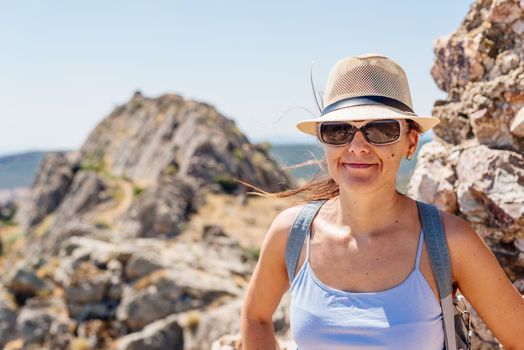 Portrait of a woman facing the camera while wearing a hat and sunglasses on a windy hilltop in Toledo, Spain