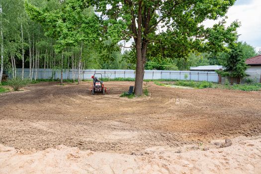 A man on a mini-excavator levels a piece of land, loosens the soil