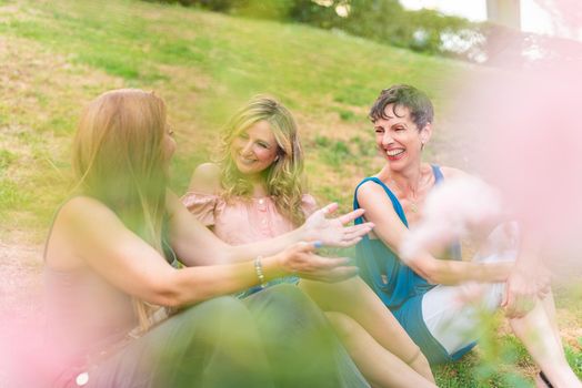 View through some leaves of mature women sitting in the park chatting. Beautiful mature women having a good time together in the park.