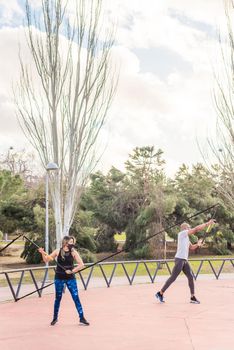 Fitness couple exercising with an elastic gym stick in the park. Multi-ethnic people exercising outside.