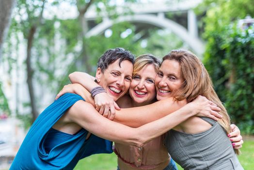 Three happy mature female friends hugging together and looking to camera. Middle aged friends sharing time together and having fun.