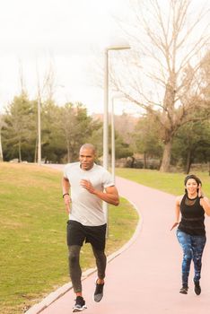 Athetic couple running on footpath in the park. Multi-ethnic people exercising outdoors.