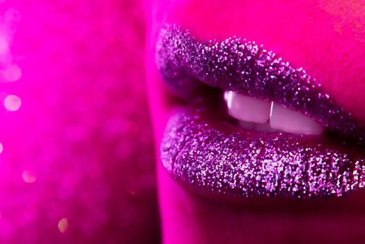 Fashion model with shiny sparkles on plump lips. Pink neon studio light. Macro view of woman with glamorous make-up. Nightlife, night club concept. Copy space