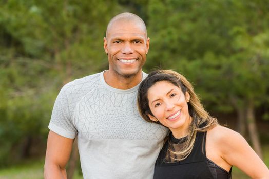 Portrait of fitness couple hugging and looking at camera. Multi-ethnic couple exercising outdoors.