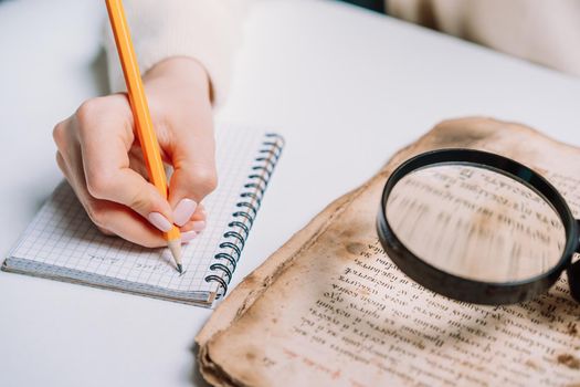 Researcher examines antique book with magnifying glass. Scientific translation of ancient literature. Studying manuscript with ancient writings. High quality