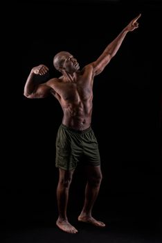 Afro-American man doing a bodybuilder pose with his arm outstretched. Muscular man with black background standing dressed only in shorts.