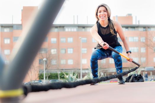 Low angle view of a fitness woman looking at camera exercising with an elastic gym stick in the park. Young adult woman exercising outside.