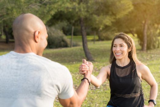 Fitness couple exercising by holding with one hand in the park. Multi-ethnic people exercising outside.