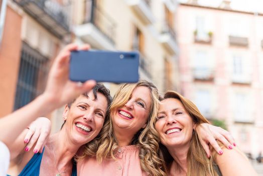 Three mature female friends hugging together taking a selfie. Middle aged friends sharing time together and having fun.