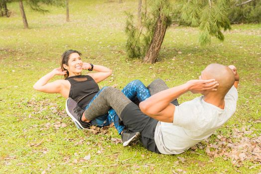 Fitness couple doing abdominal excersise holding by the legs. Couple doing exercise outdoors together.