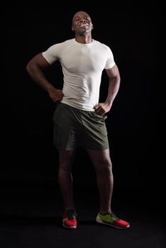 African American man standing looking at camera with fists on waist. Muscular adult male in sportswear in a studio with black background.