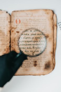 Woman researcher in gloves explores antique book with magnifier. Scientific translation of literature. Investigating manuscript with ancient writings. High quality