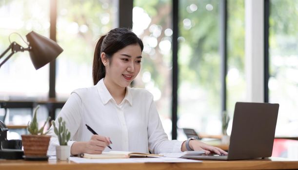 Beautiful young asian woman sitting at coffee shop using laptop. Happy young businesswoman sitting at table in cafe with tab top computer..