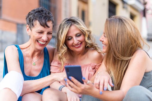 Three cheerful mature friends together using cell phone and laughing. Middle aged friends sharing time together and having fun.