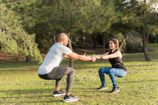 Fitness couple exercising by holding hands in the park. Multi-ethnic people exercising outside.