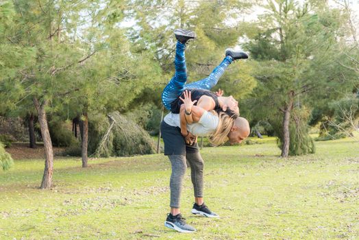 Fitness couple doing back to back lifting exercise in the park. Multi-ethnic people exercising outdoors.