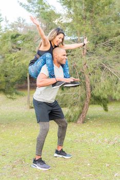 Sportswoman sitting on the shoulders of sportsman exercising and having fun. Couple doing exercise outdoors together.