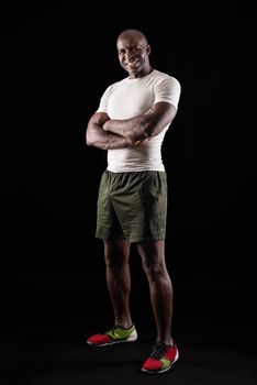 Portrait of african american sportsman posing with crossed arms at studio. Athlete adult man wearing spotswear standing looking at camera on a black background.